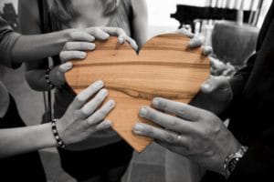 close up wooden heart held by three people