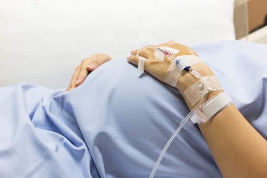 pregnant-belly woman on hospital bed holding pregnant belly with IV in hand