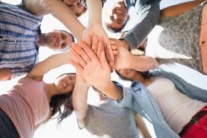 upward view of people grouped in circle with hands in the middle