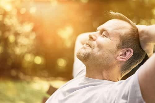 man on park bench peacefully leaning head back in his hands